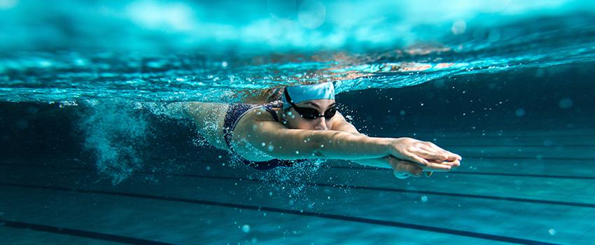 Swimmer swimming in indoor pool with goggles on.